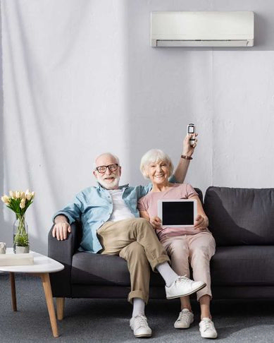 Lächelndes älteres Paar zeigt digitales Tablet und hält Fernbedienung der Klimaanlage zu Hause in der Hand